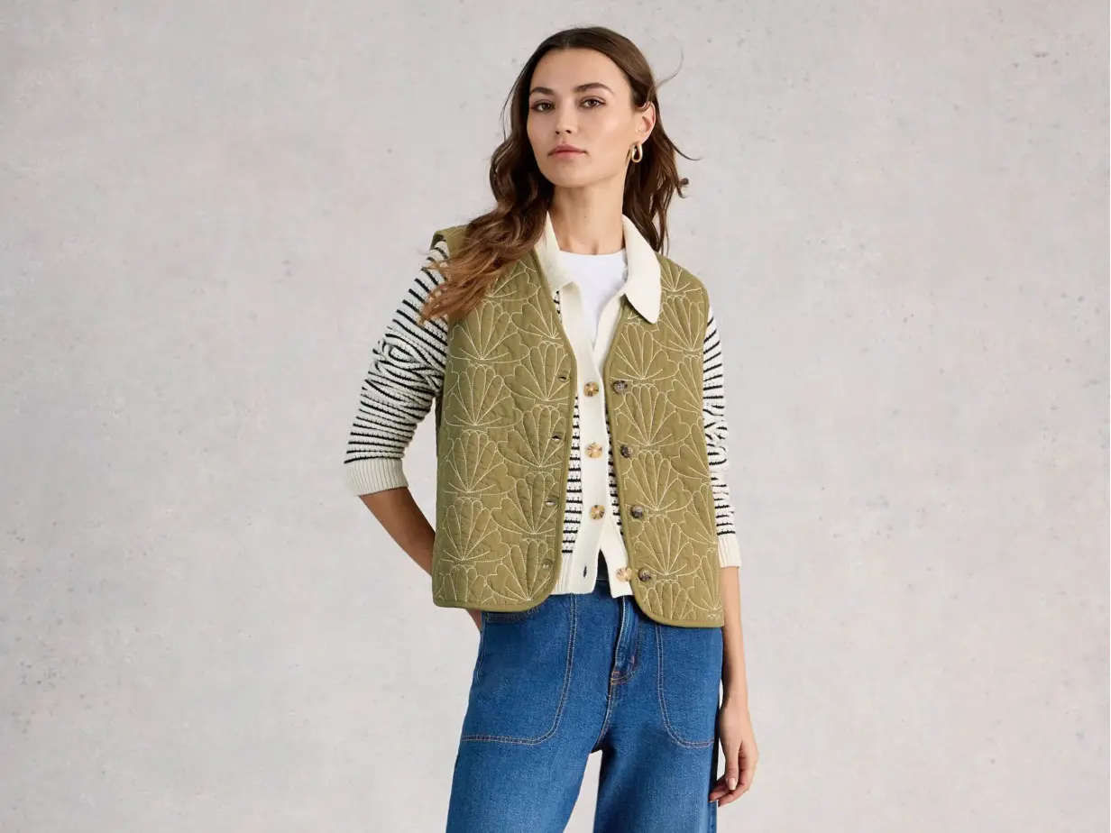 Woman wearing green gilet over striped cardigan and blue jeans 