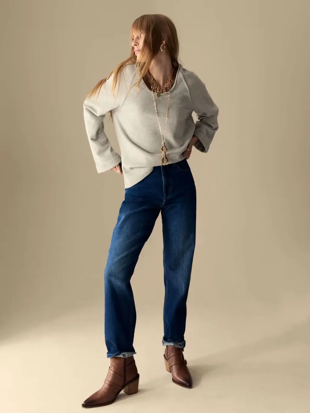Woman wearing a grey sweatshirt with indigo straight-leg jeans and brown cowboy boots