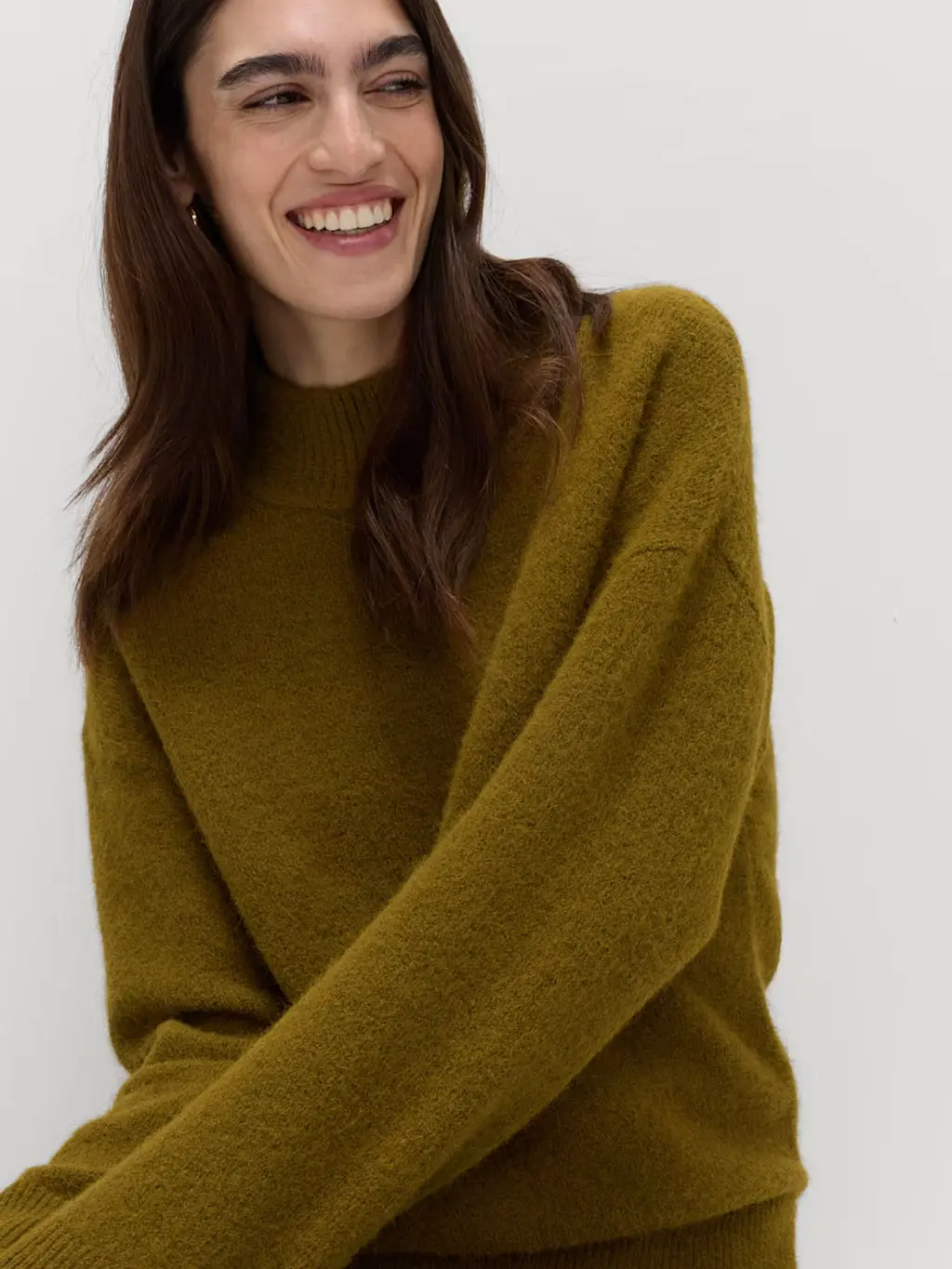 Woman wearing a green funnel-neck jumper with gold jewellery