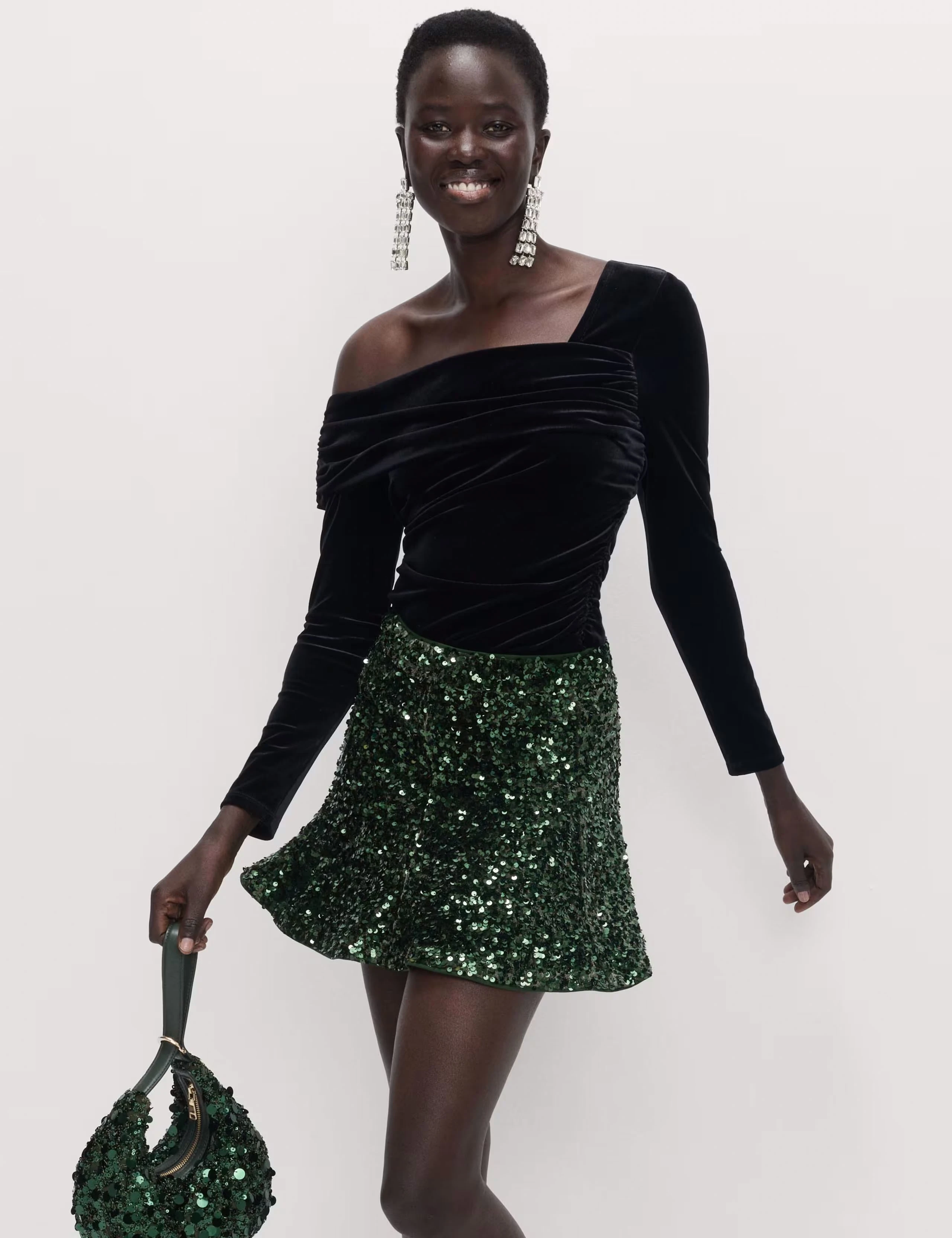 Woman wearing a black asymmetric top with a green sequinned mini skirt