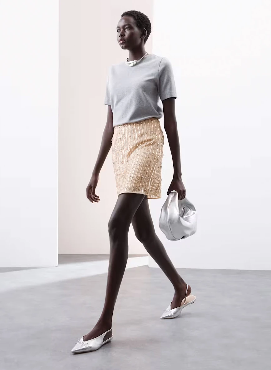 Woman wearing a grey T-shirt, a peach sequinned mini skirt and silver pumps