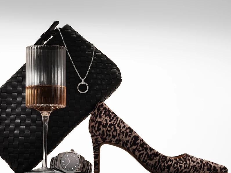 Assorted birthday present ideas, including a woven bag, a glass of pink champagne, a necklace, a watch and a leopard-print court shoe