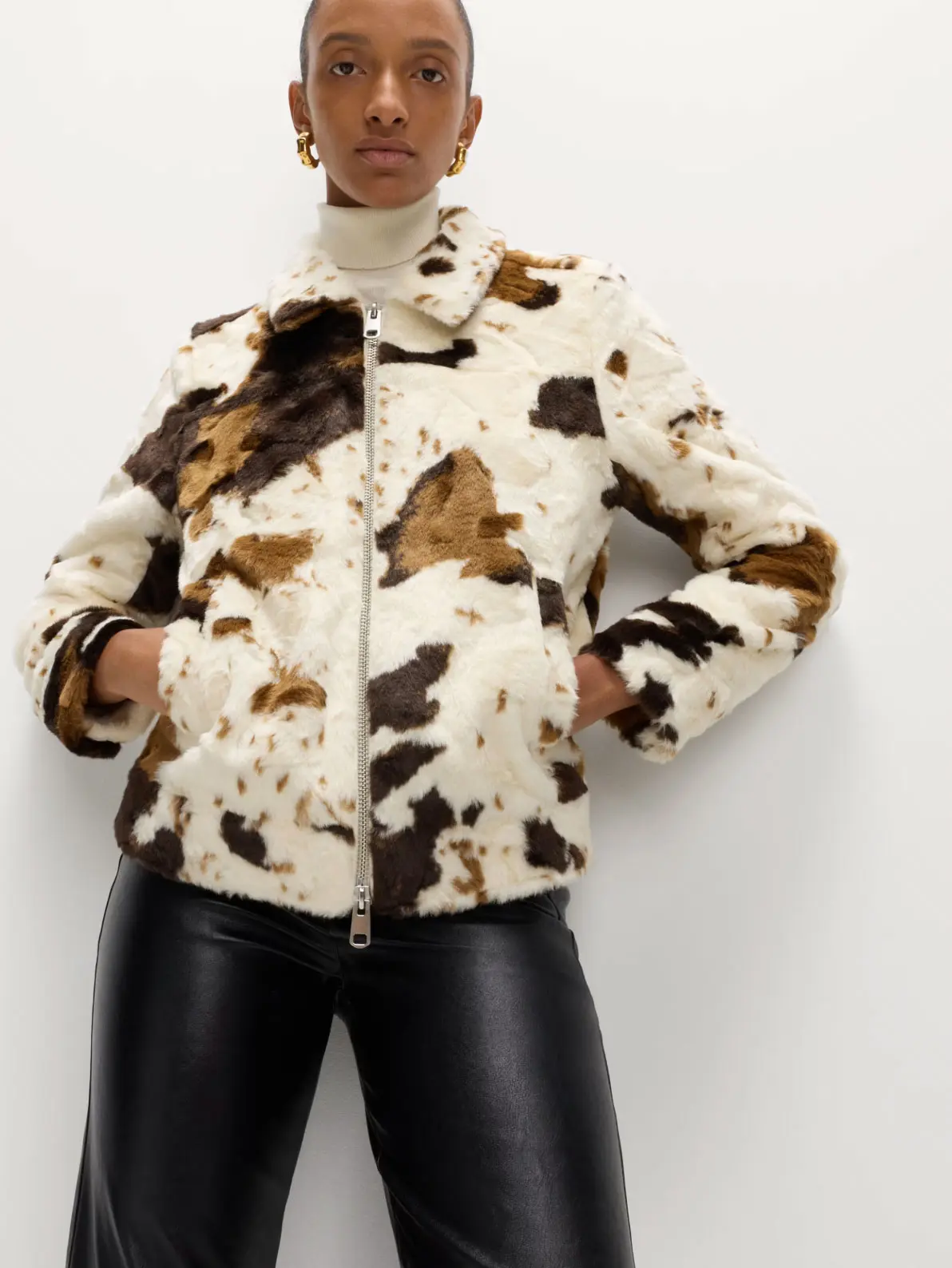 Woman wearing neutral cow print faux-fur jacket and pleather black trousers