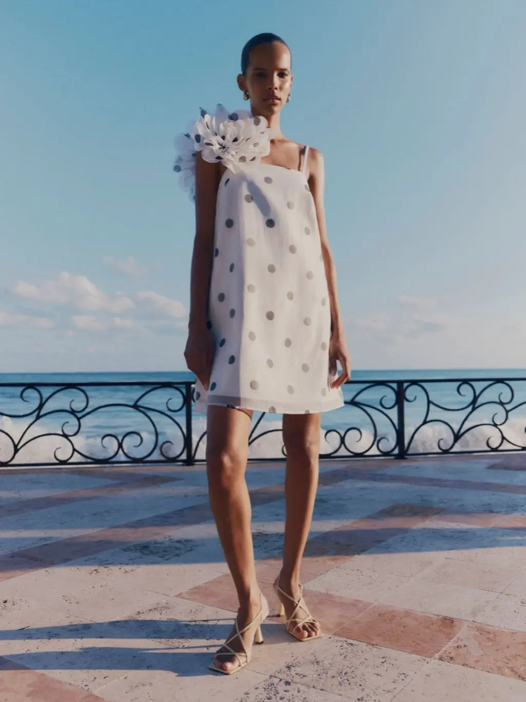 A woman wears a short polka dot shift dress and neutral sandals
