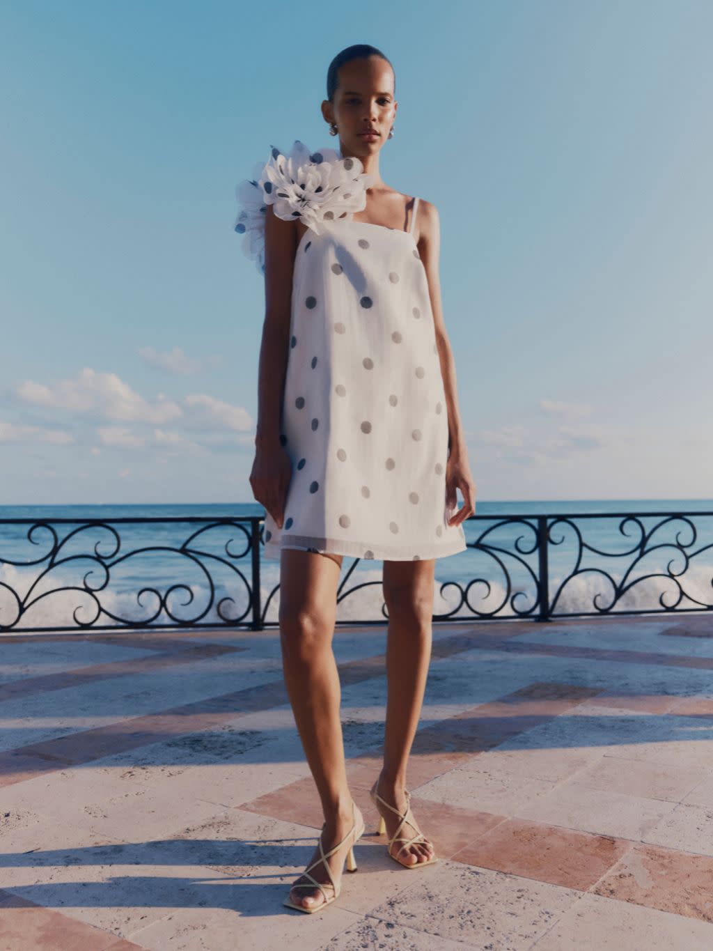 A woman wears a short polka dot shift dress and neutral sandals