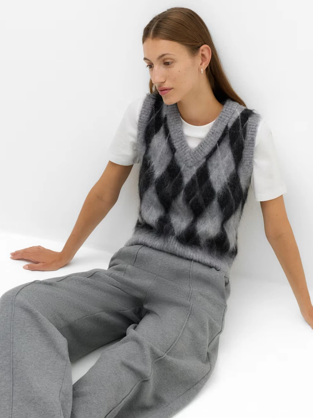 Woman wearing a pair of grey joggers with an argyle sweater vest and white T-shirt.