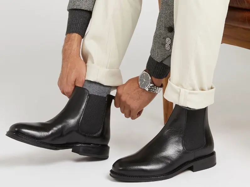 A close up of a man putting Chelsea boots on