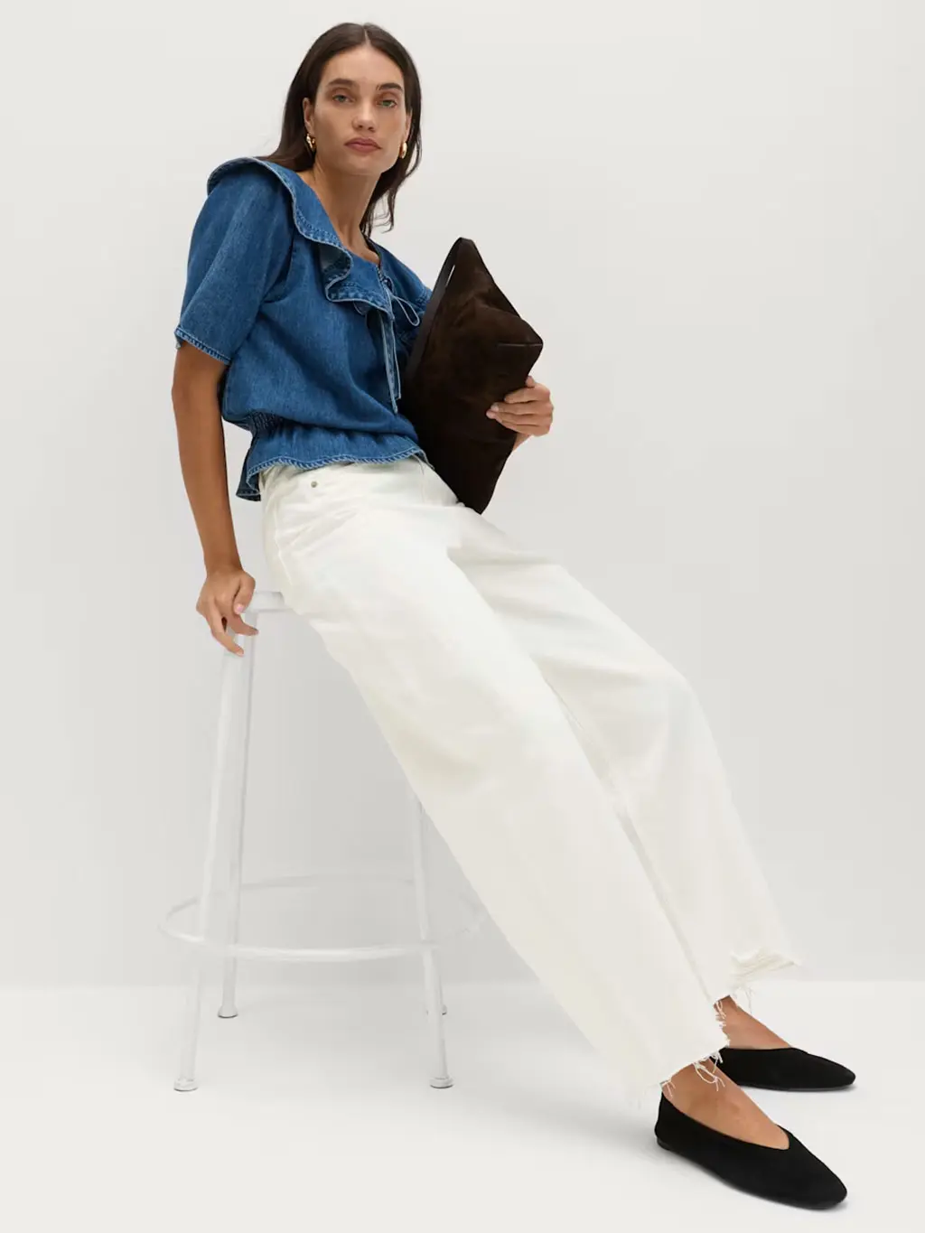 Woman wearing a denim blouse with white barrel-leg jeans and black pumps