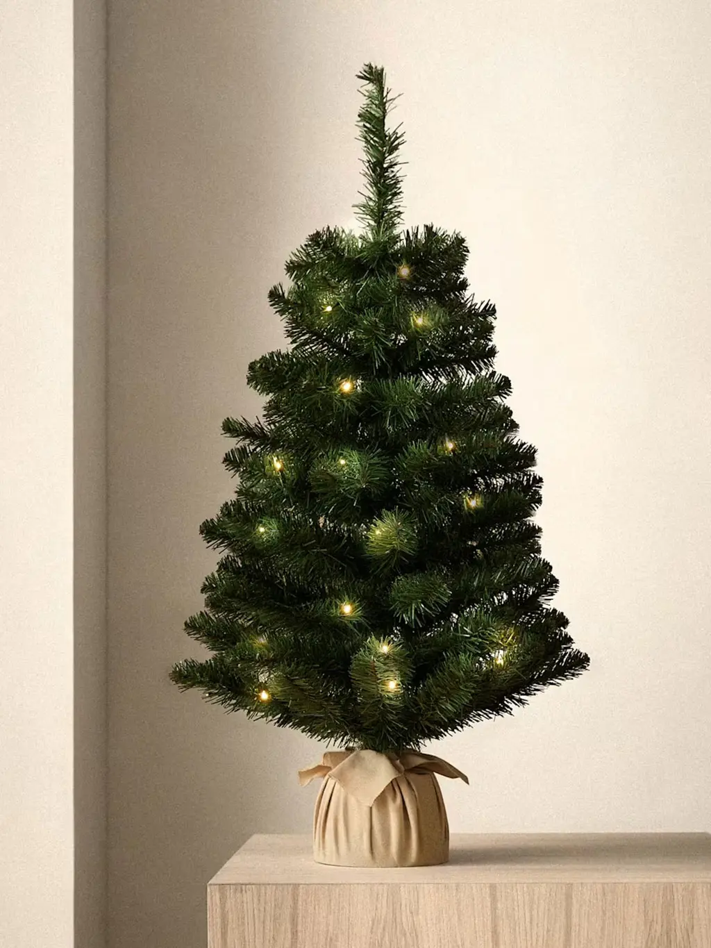 Small artificial spruce Christmas tree with warm white lights and hessian pot.
