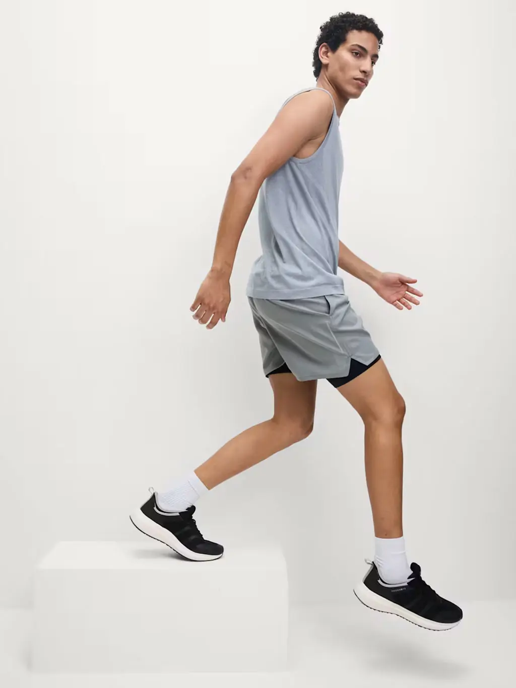 Man wearing a grey vest with shorts and black trainers