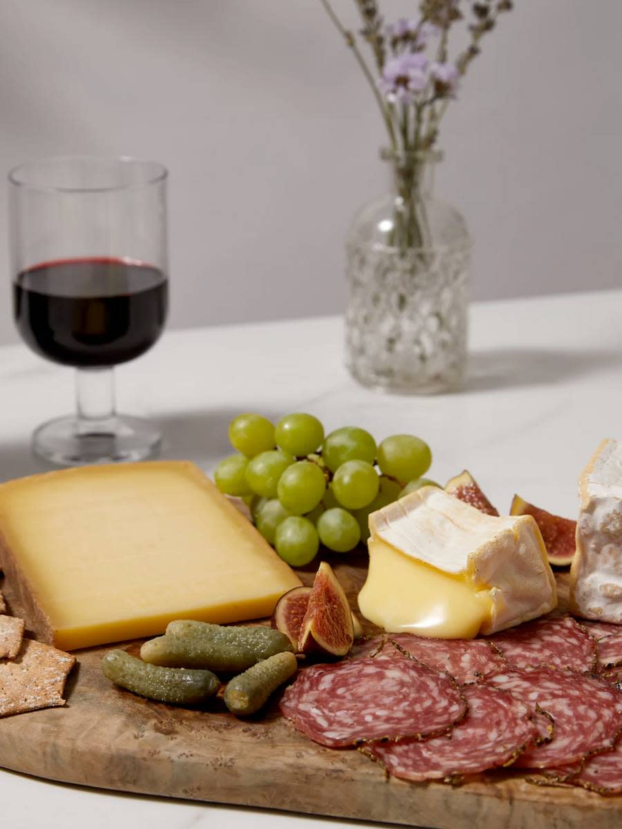 Selection of sliced cheese, meats, grapes and a glass of wine. Shop food hampers