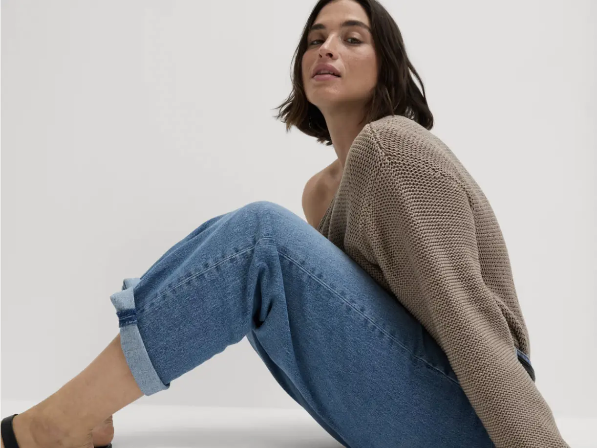 Woman sitting down wearing blue jeans and brown jumper