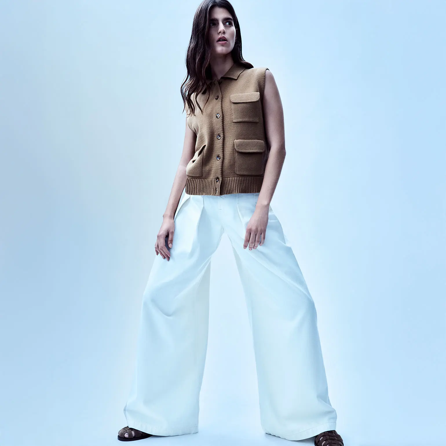 Woman wearing ecru palazzo jeans and a tan knitted waistcoat