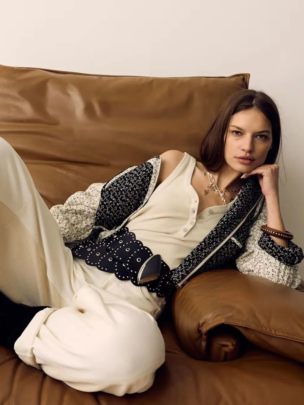 Woman wearing a cream vest and jeans with an oversized studded belt, quilted jacket and black slouchy boots
