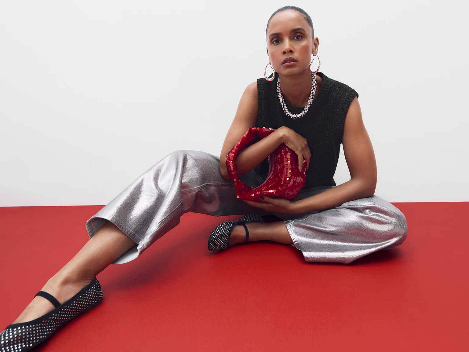 Woman wearing black sleeveless top, silver jeans and a red sequin grab bag
