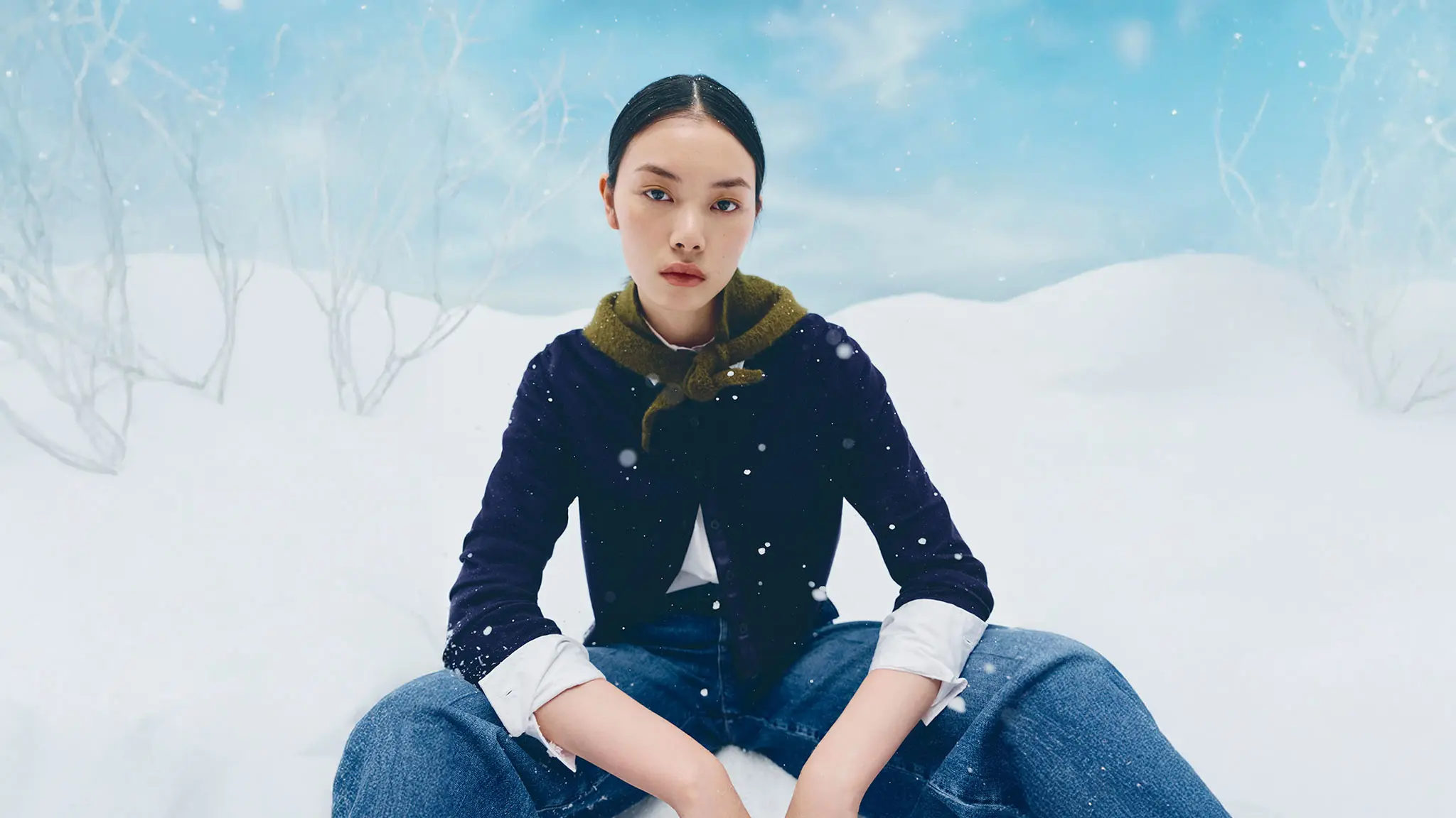 Woman wearing a blue cardigan, white shirt, blue jeans and a green scarf