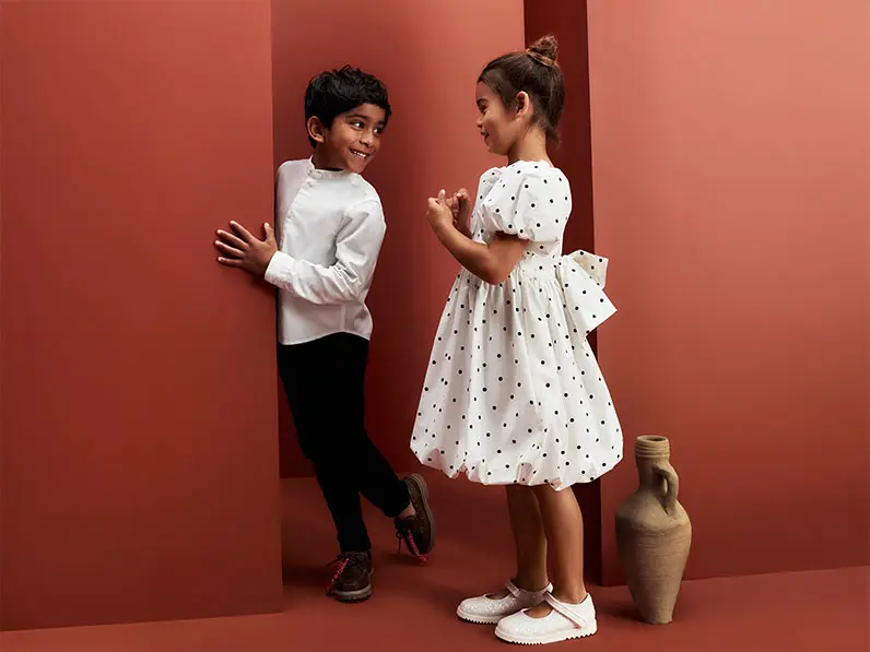 Girl and boy wearing smart occasionwear against red backdrop
