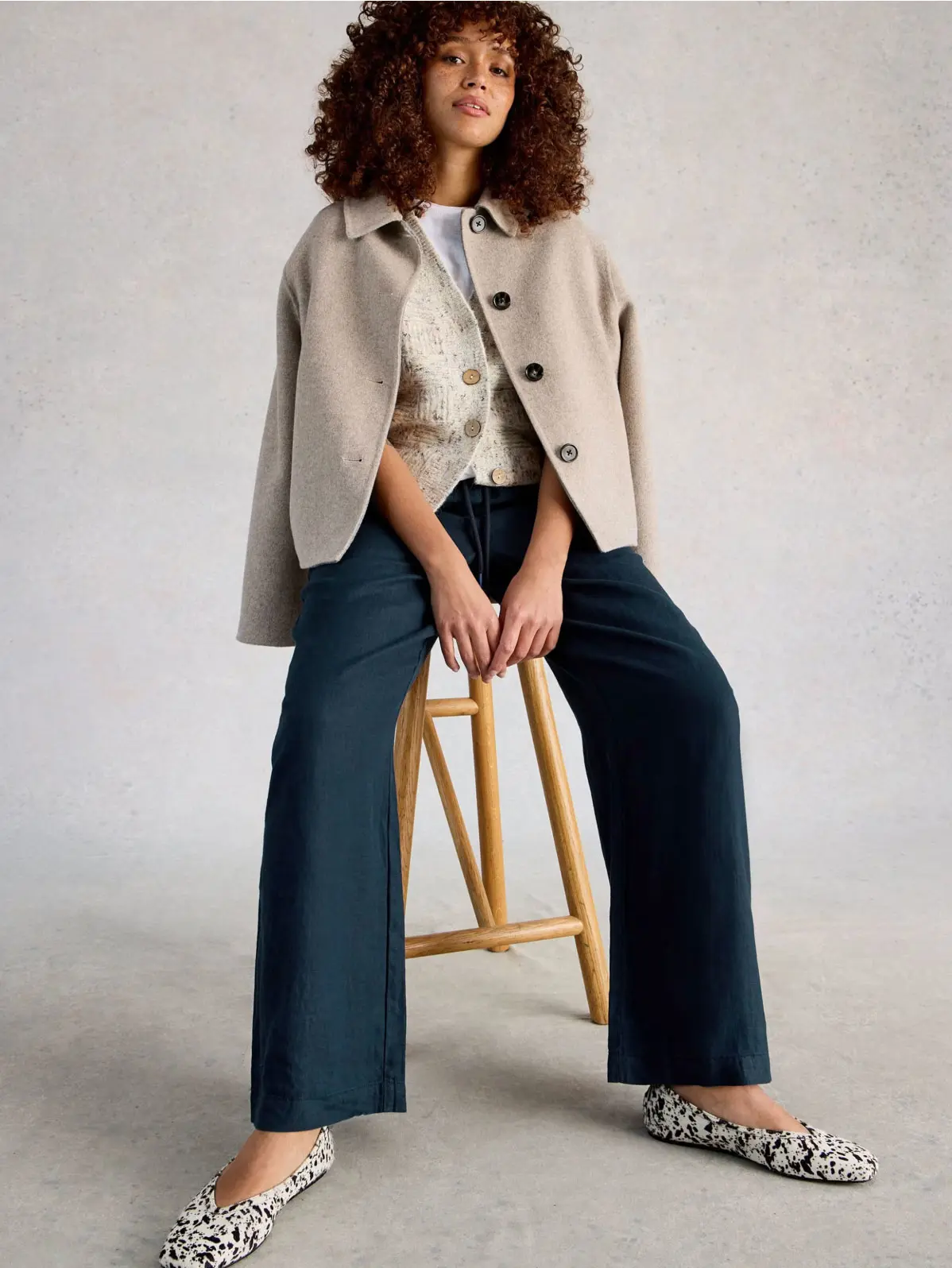 Woman wearing white T-shirt, cream cardigan, beige jacket, navy linen trousers and printed flats 