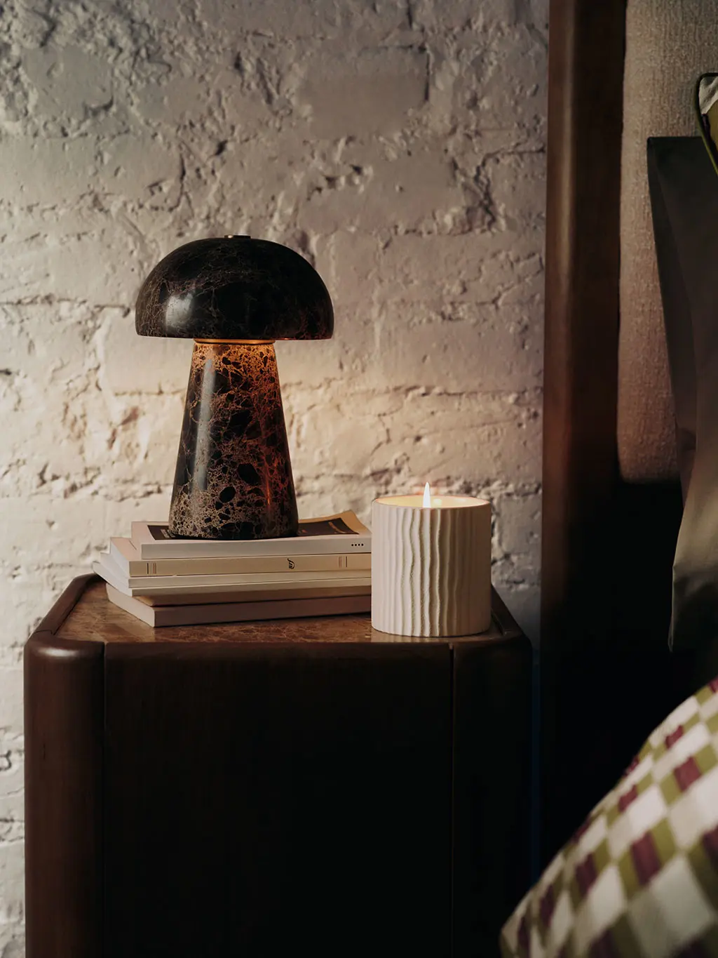 Neutral bedside setting with a dark wooden table, swirly lamp and scented candle.