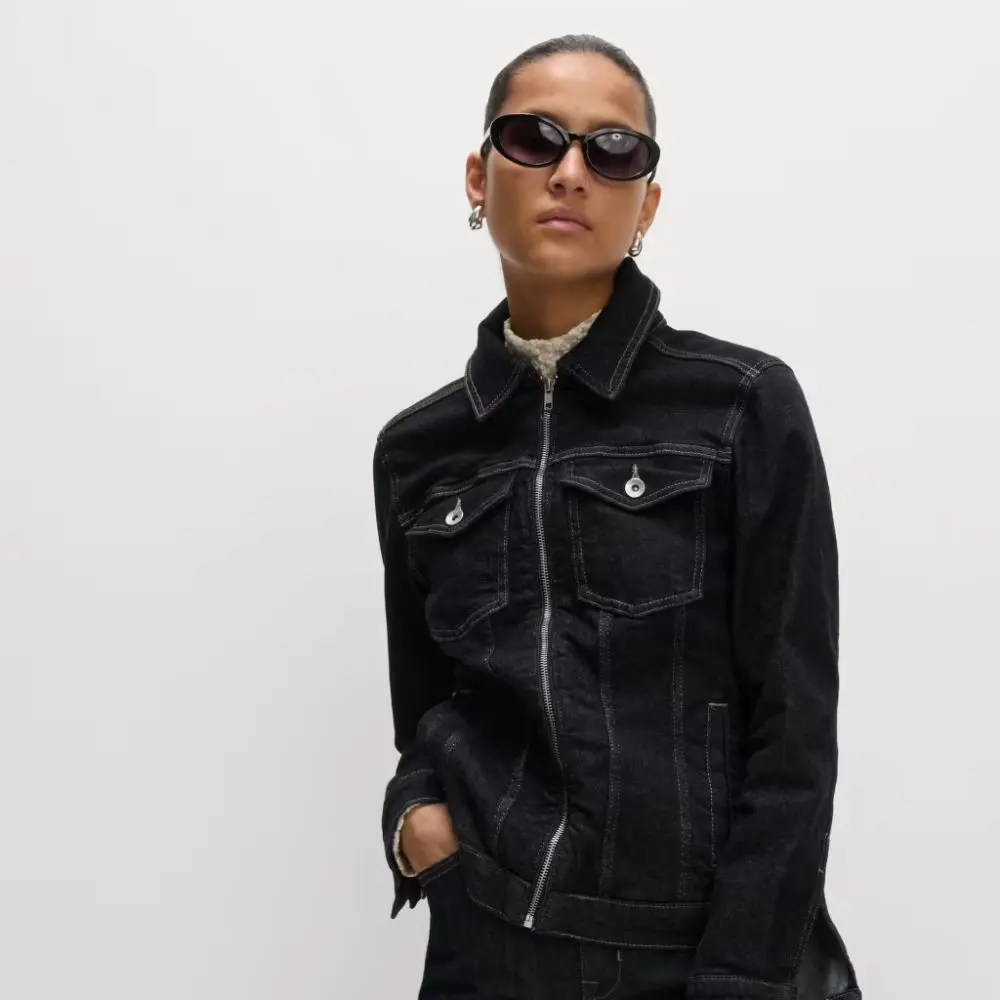 A woman wearing a dark denim jacket and sunglasses