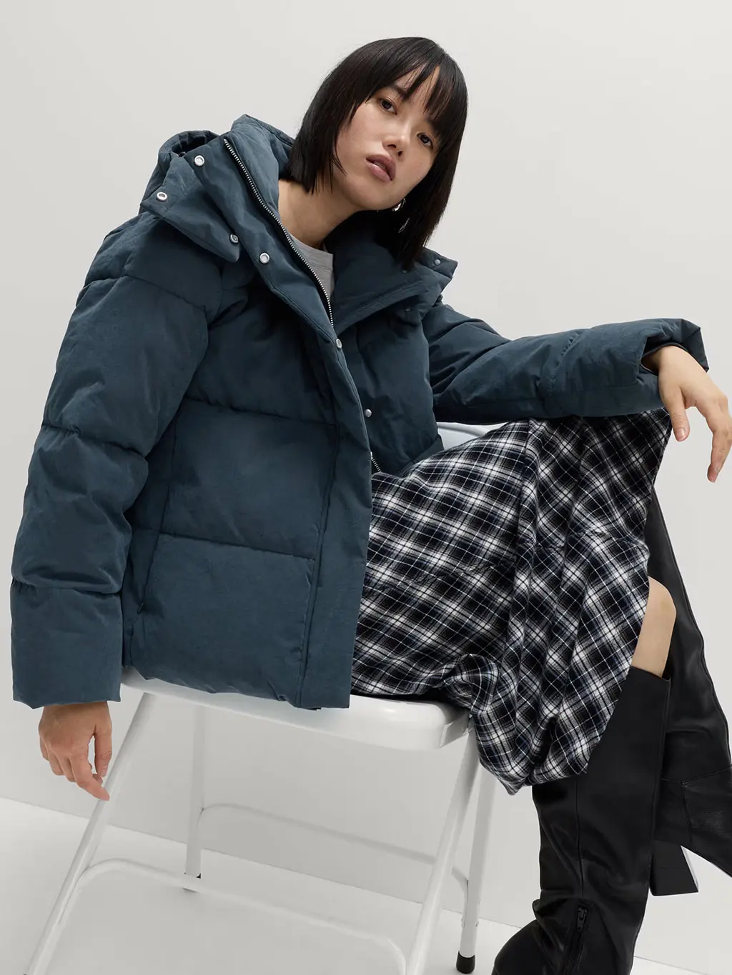 Woman wearing a grey puffer jacket with a checked skirt and knee-high boots