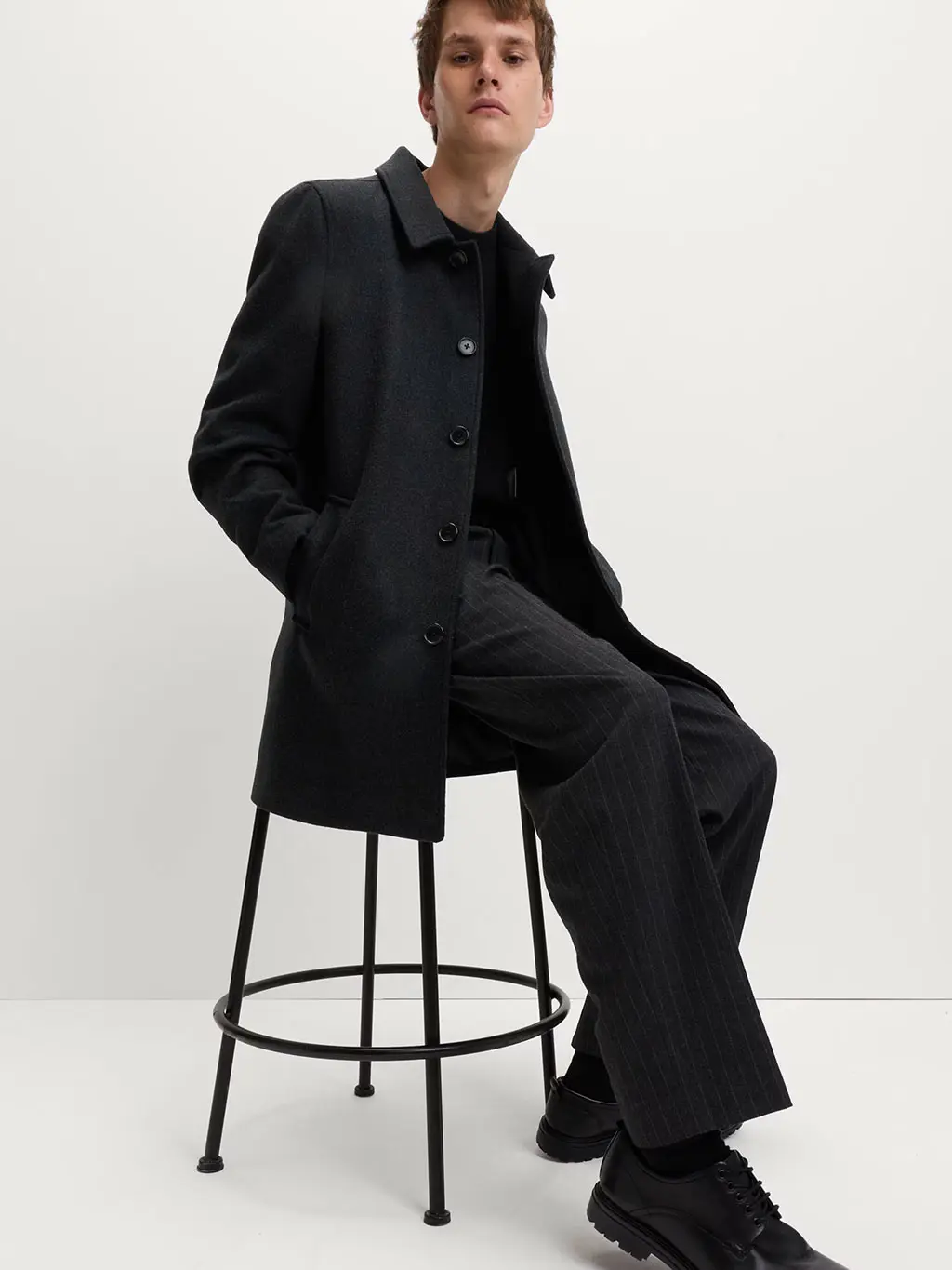 Man wearing a wool overcoat with a black jumper and smart trousers and shoes.