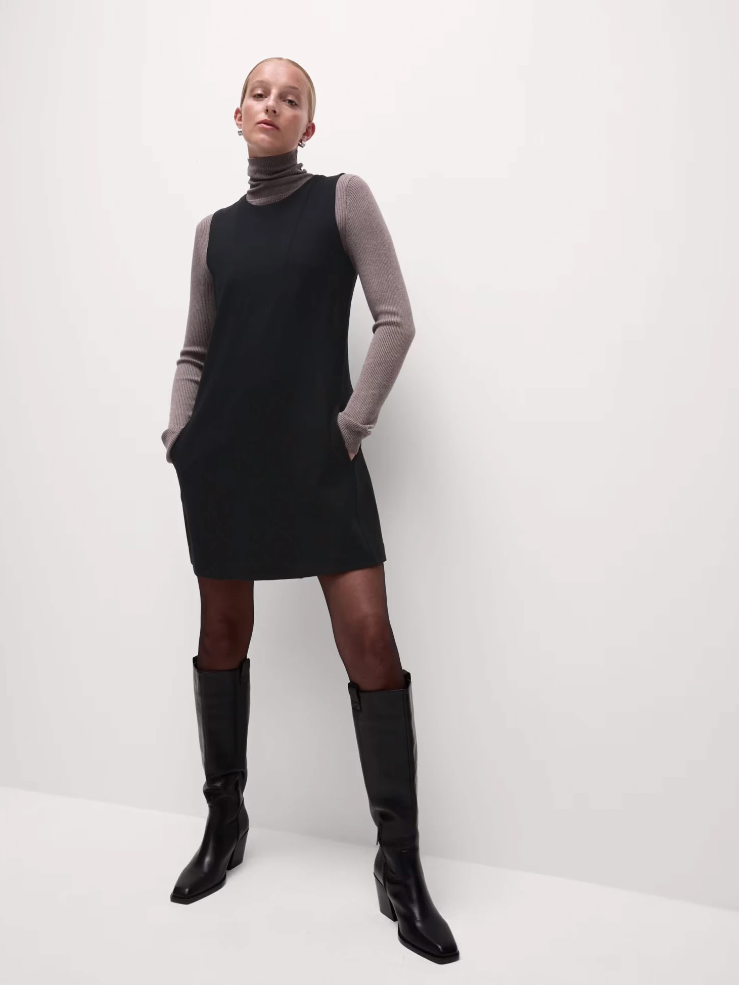 Woman wearing black mini shift dress over a polo-neck top