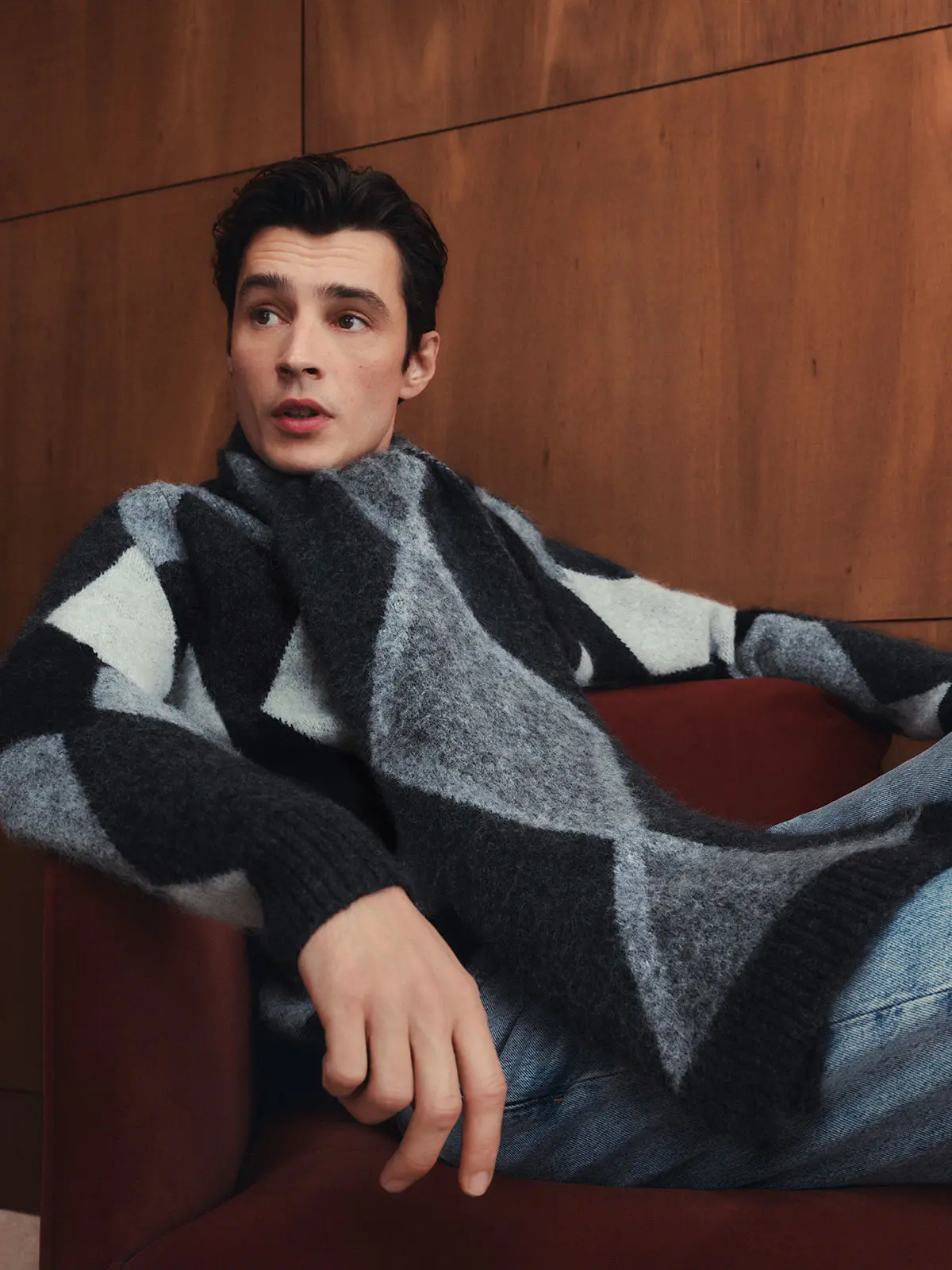 Man wearing grey and black argyle jumper with matching scarf and blue jeans