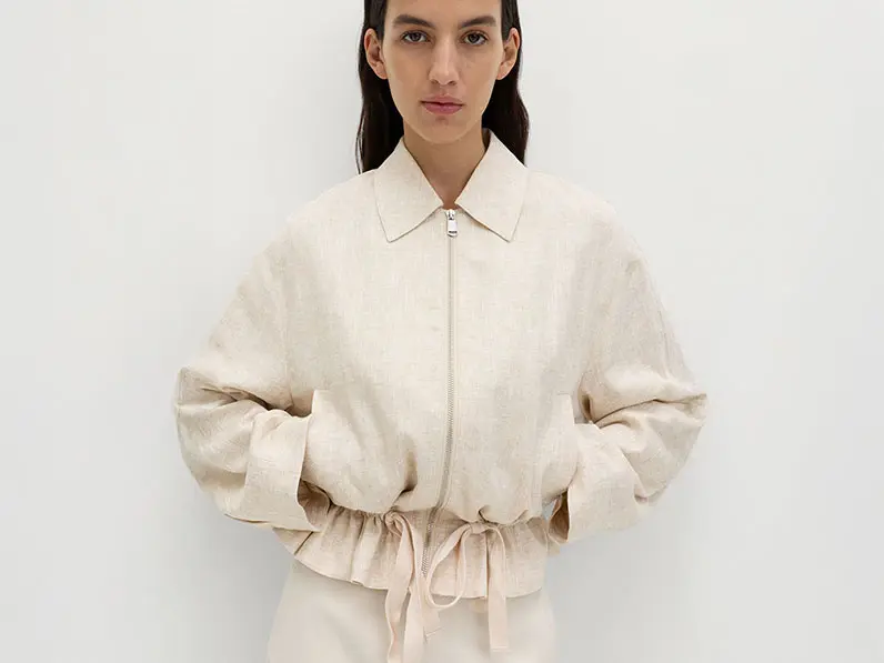 Woman wearing a neutral jacket with white trousers