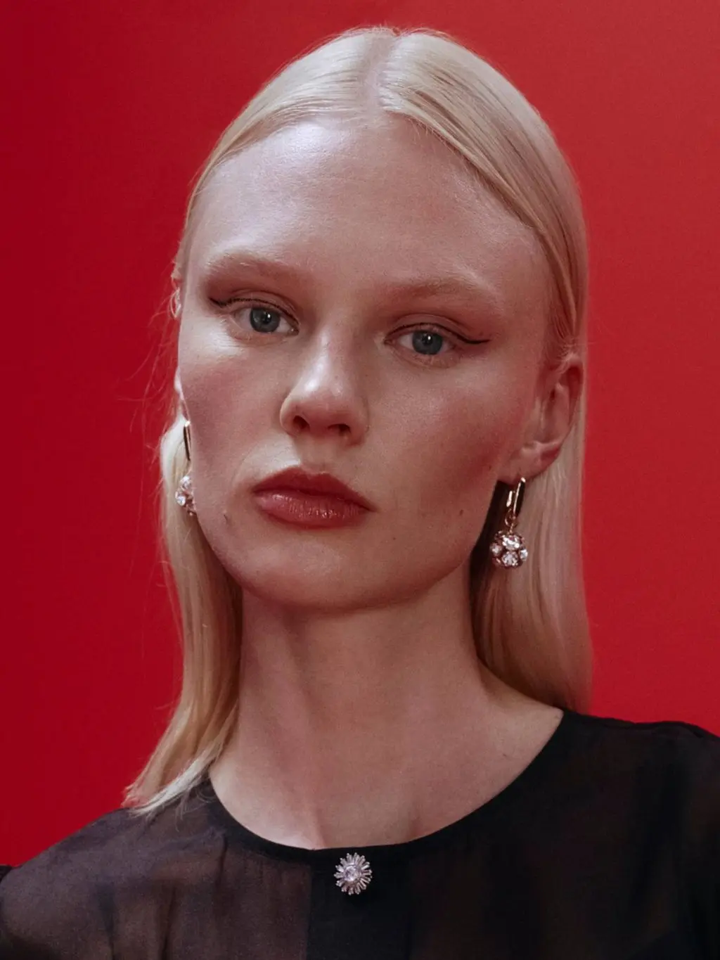 A woman has graphic eyeliner, and wears sparkly earrings and a black top