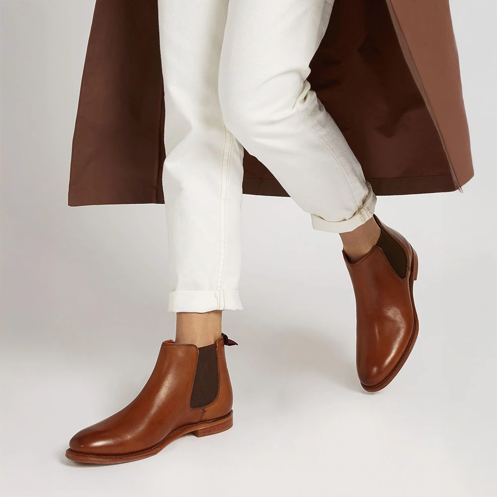 Woman wearing tan coat, white jeans and brown Chelsea boots