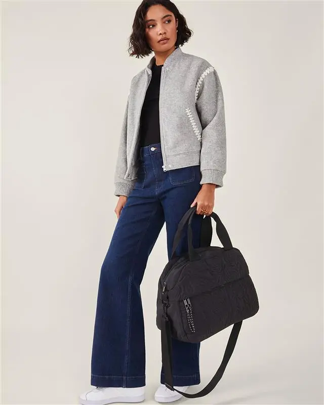 Woman in grey jacket and blue jeans holding black weekend bag