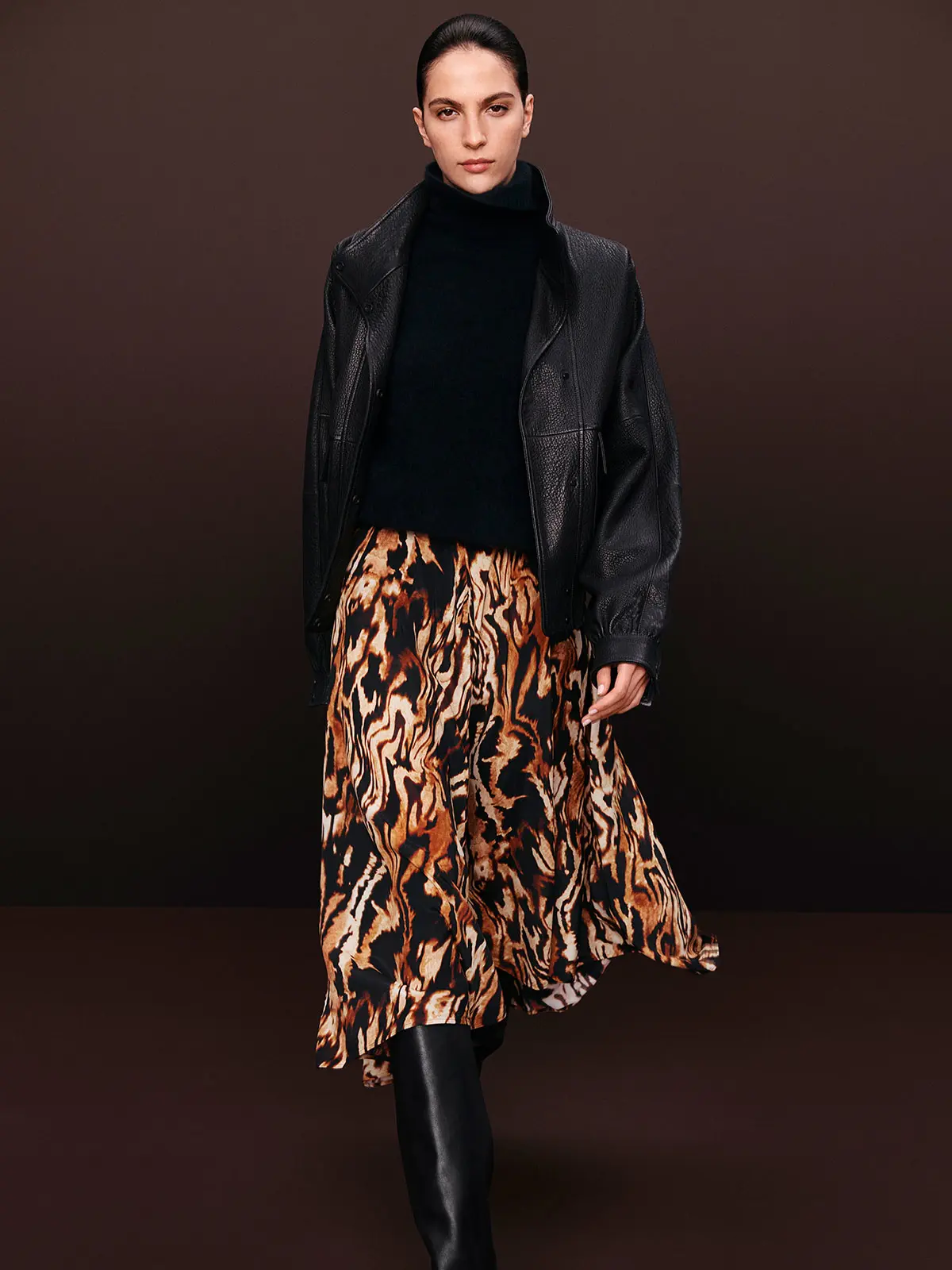 Woman wearing black leather jacket with printed skirt and tall black boots 
