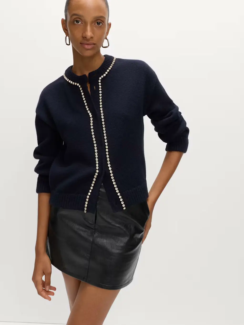 Woman wearing a black faux-leather mini skirt with a beaded cardigan and hoop earrings