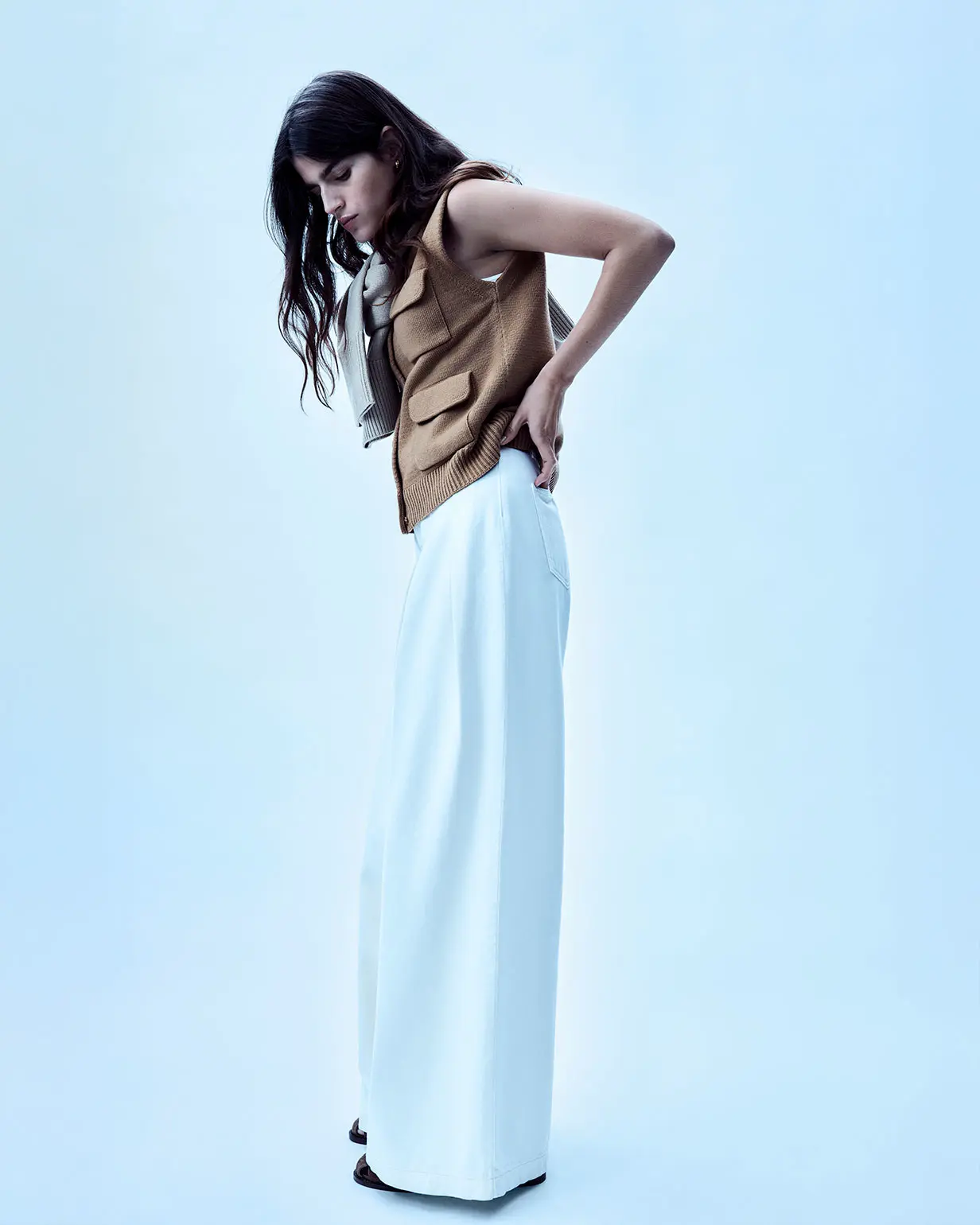 Woman wearing ecru palazzo jeans and a tan knitted waistcoat