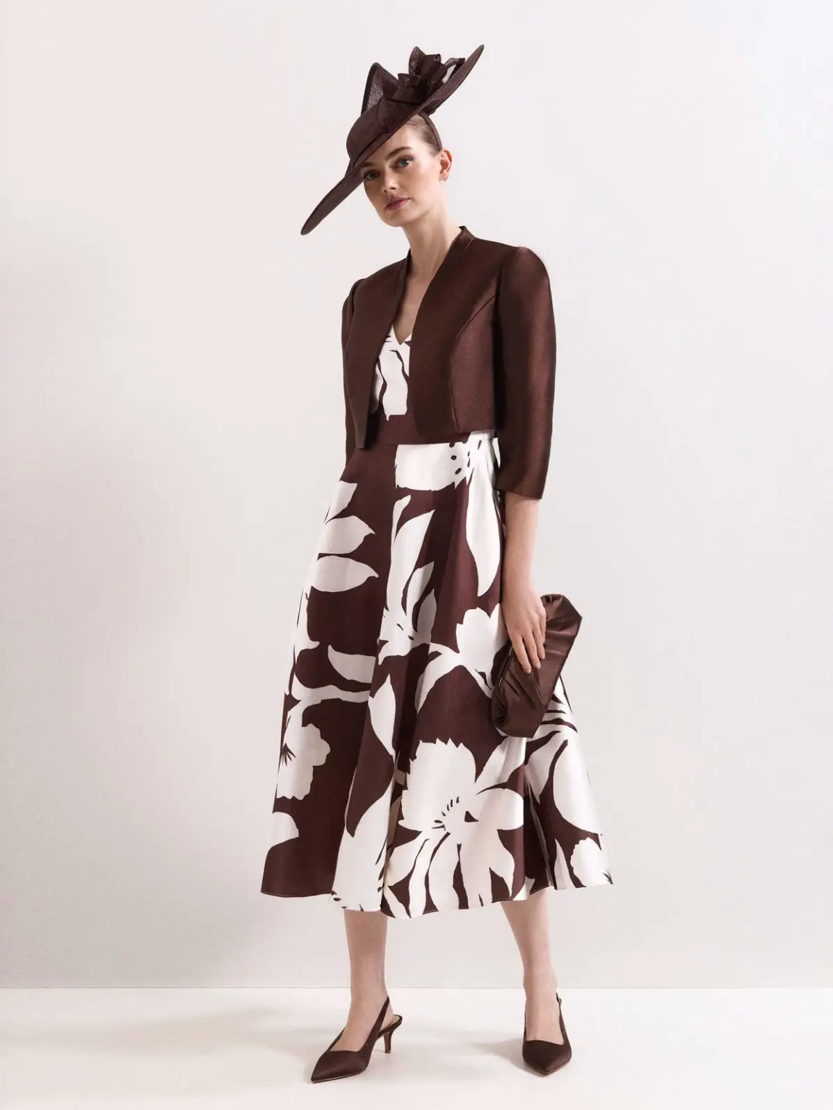Woman wearing brown and white floral dress with a fascinator and heels 