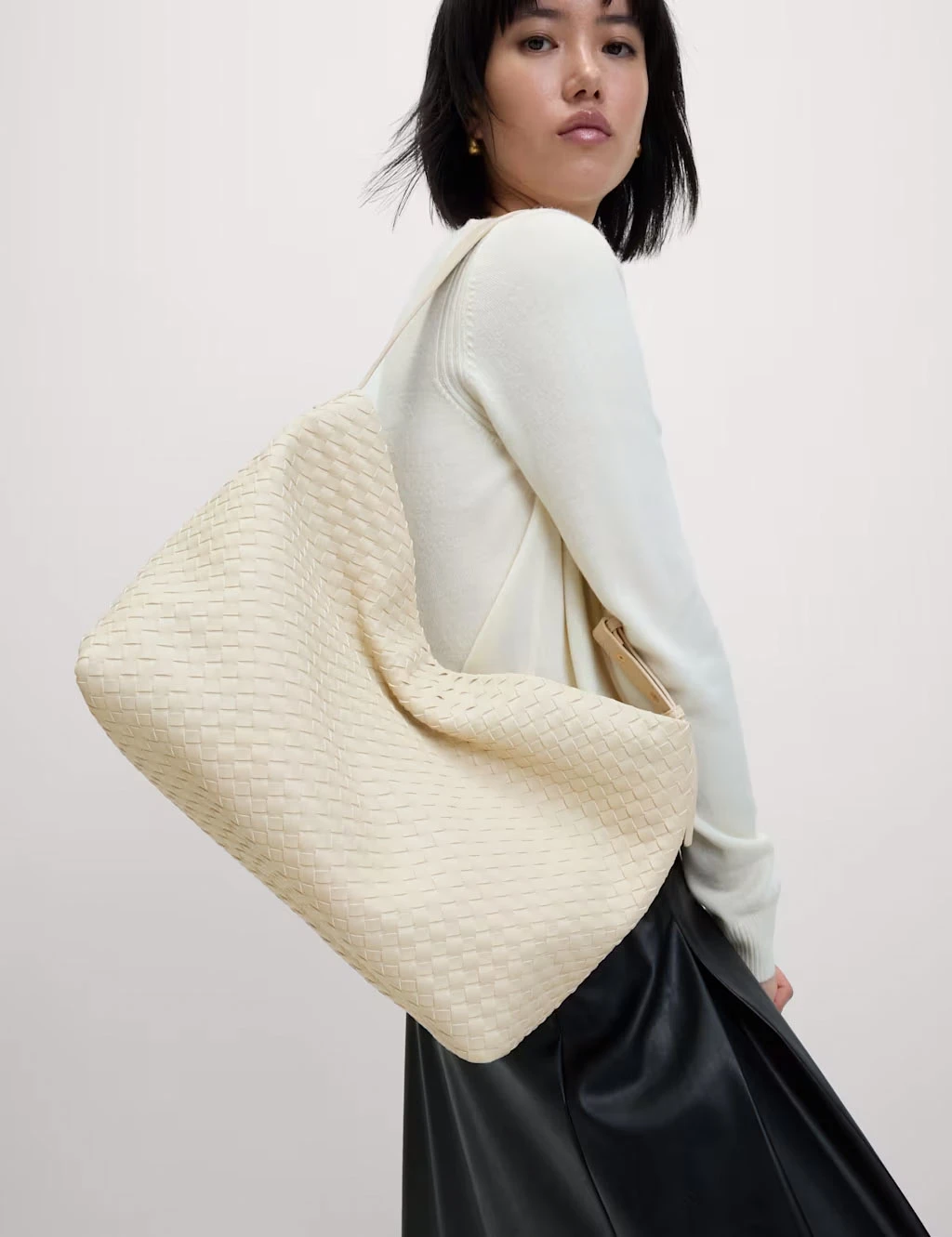 Woman wearing a white jumper and black skirt with a white woven tote bag.