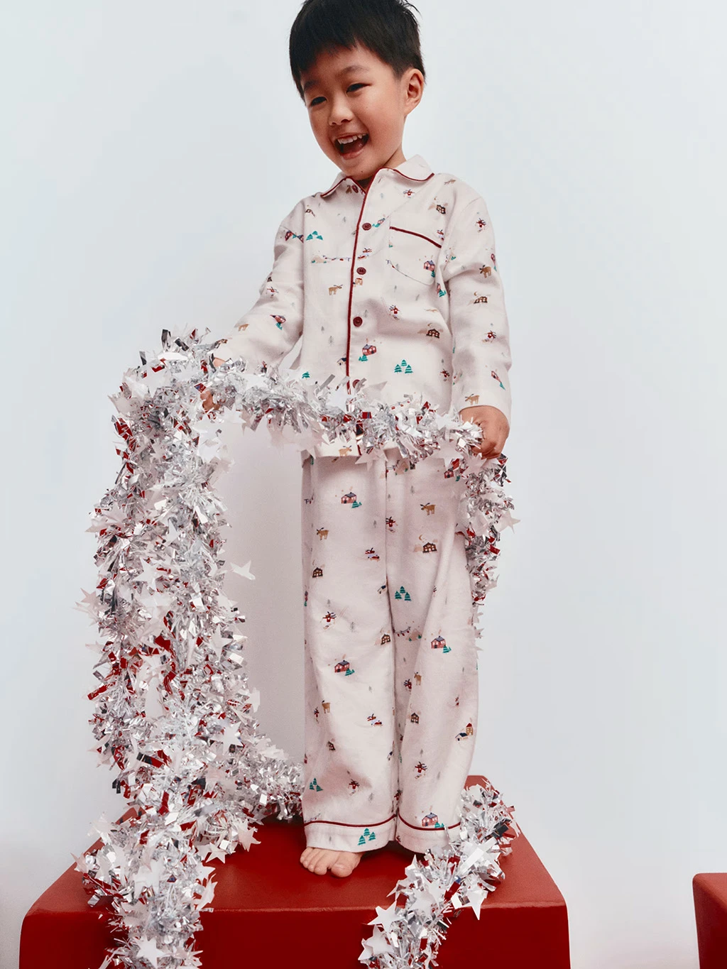 Child in a pair of long Christmas pyjamas holding tinsel.