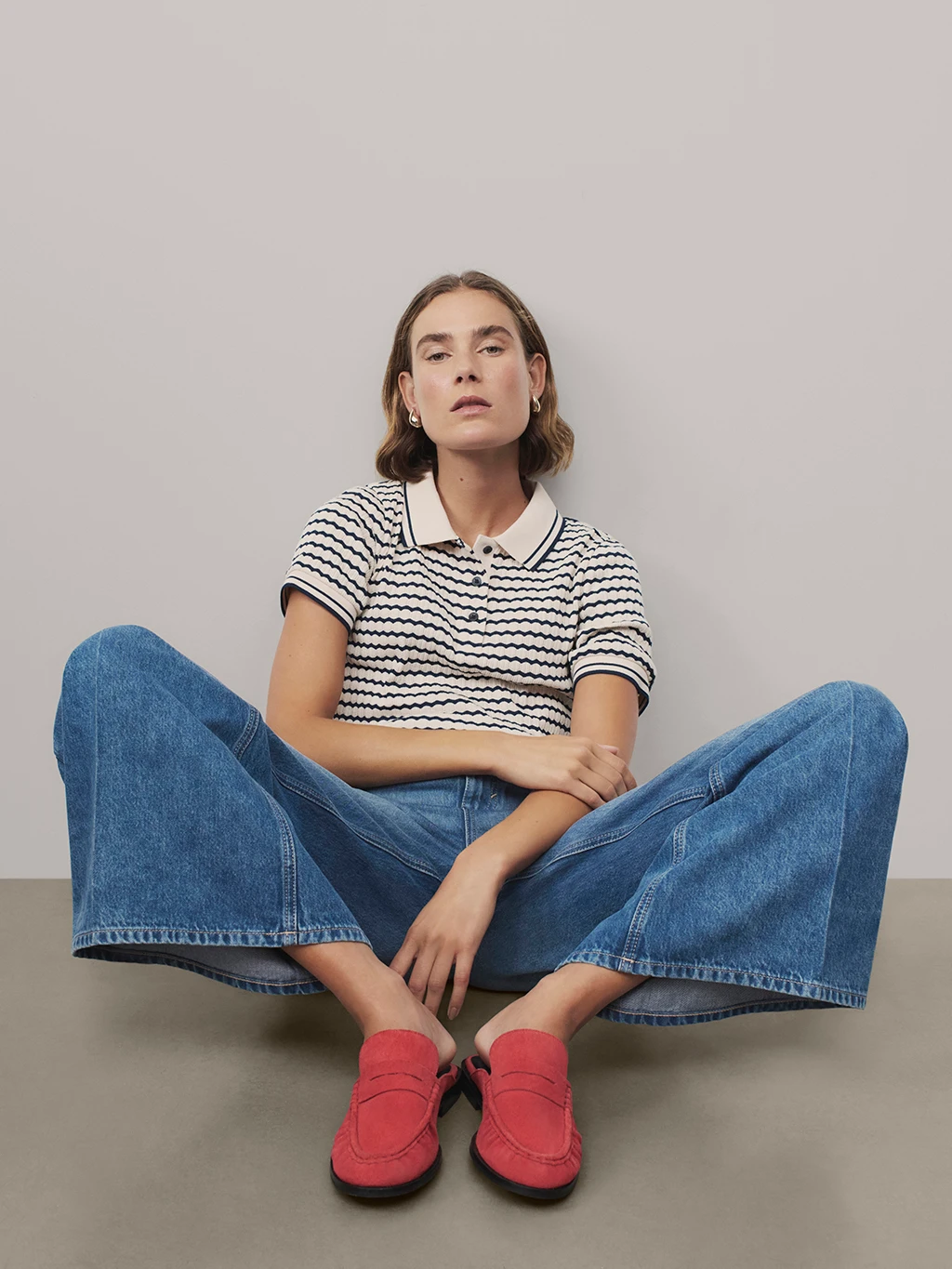 Woman wearing black and white striped polo shirt, blue jeans and red loafers