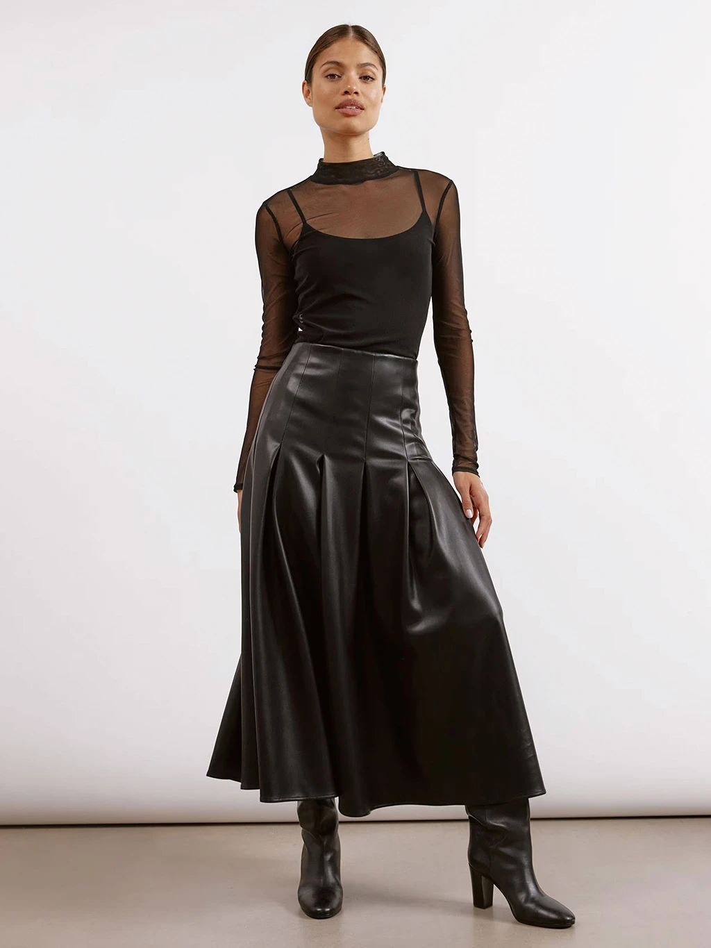 Woman wearing black sheer mesh top, black leather-look pleated skirt and a pair of black boots