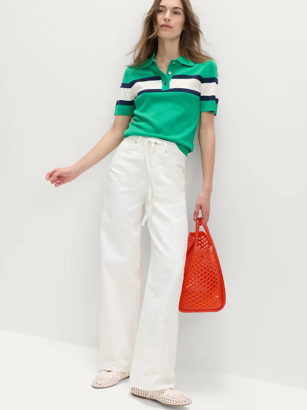 Woman wearing a green jumper and white wide-leg jeans with pumps and a red bag