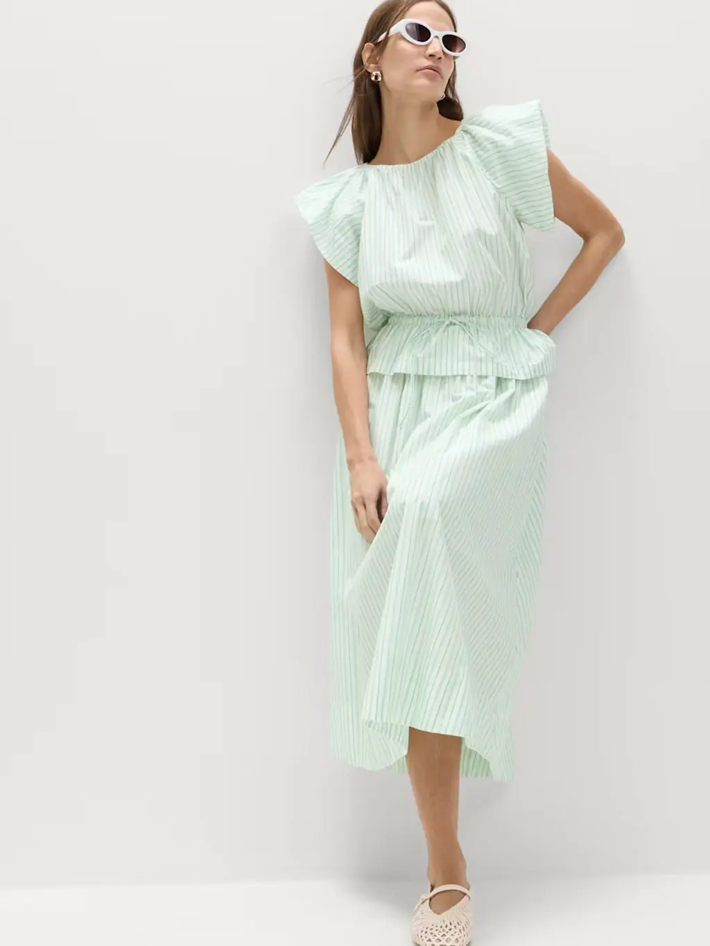 Woman wearing striped green two-piece set of a blouse and a skirt with white sunglasses and pumps
