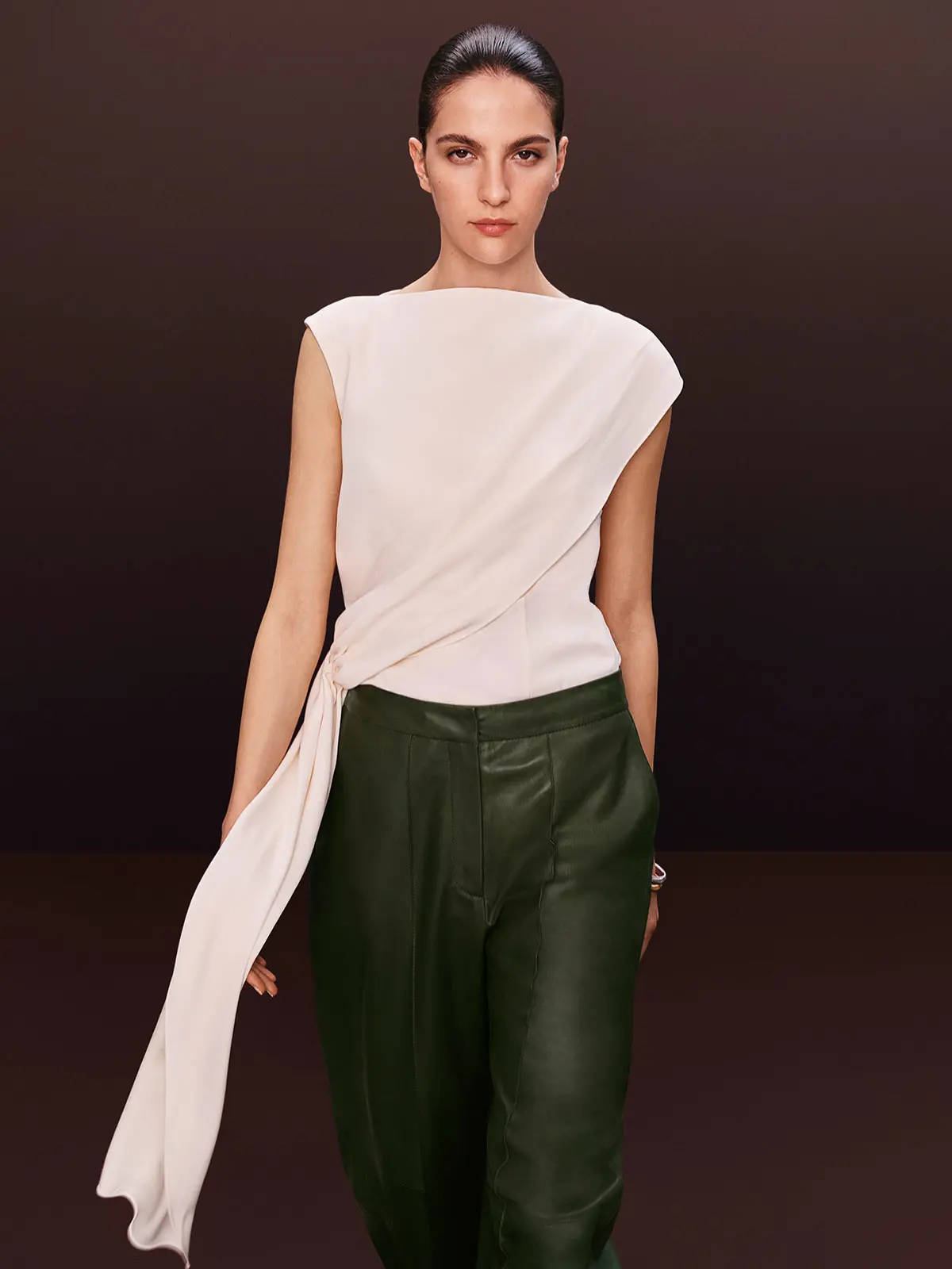 Woman wearing white draped top with green leather trousers