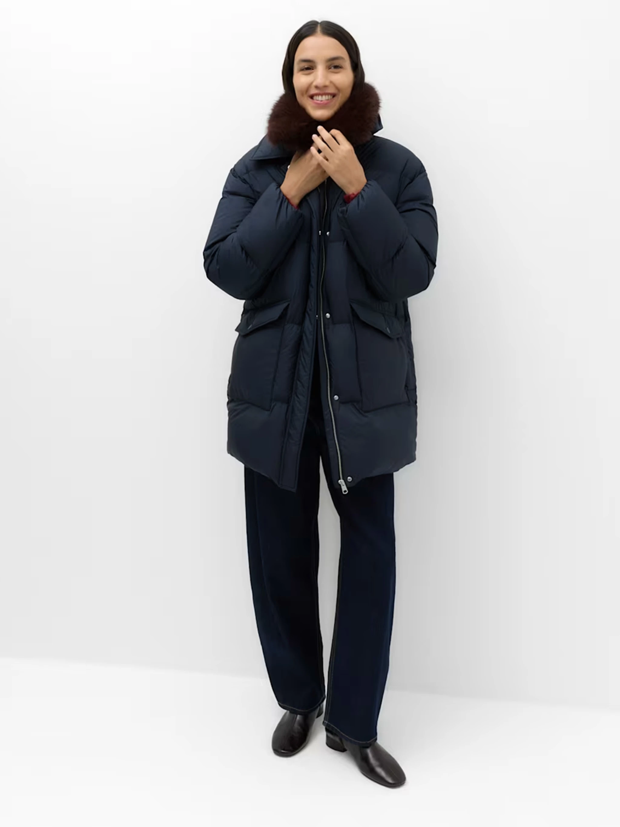 Woman wearing straight black trousers and a longline navy puffer coat with a faux fur collar.