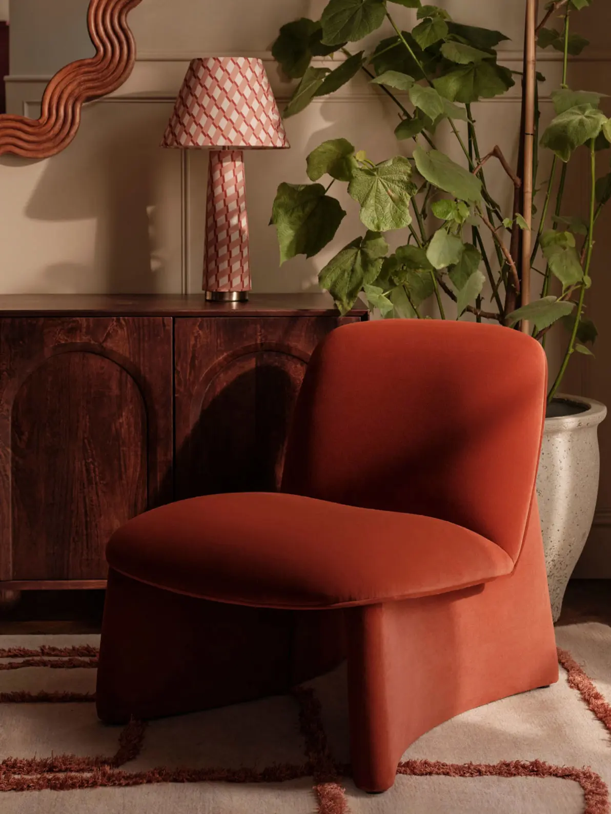 Image of burnt orange chair in front of wood cabinet, pink checked lamp and plant