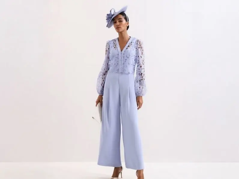A woman wears a lilac lace jumpsuit and fascinator