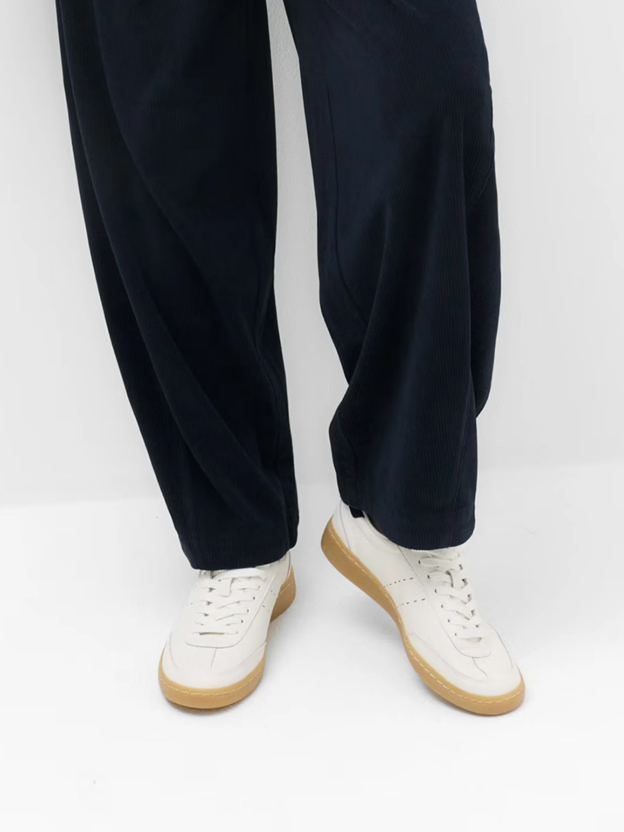 Close up of a woman wearing blue barrel trousers and white trainers.