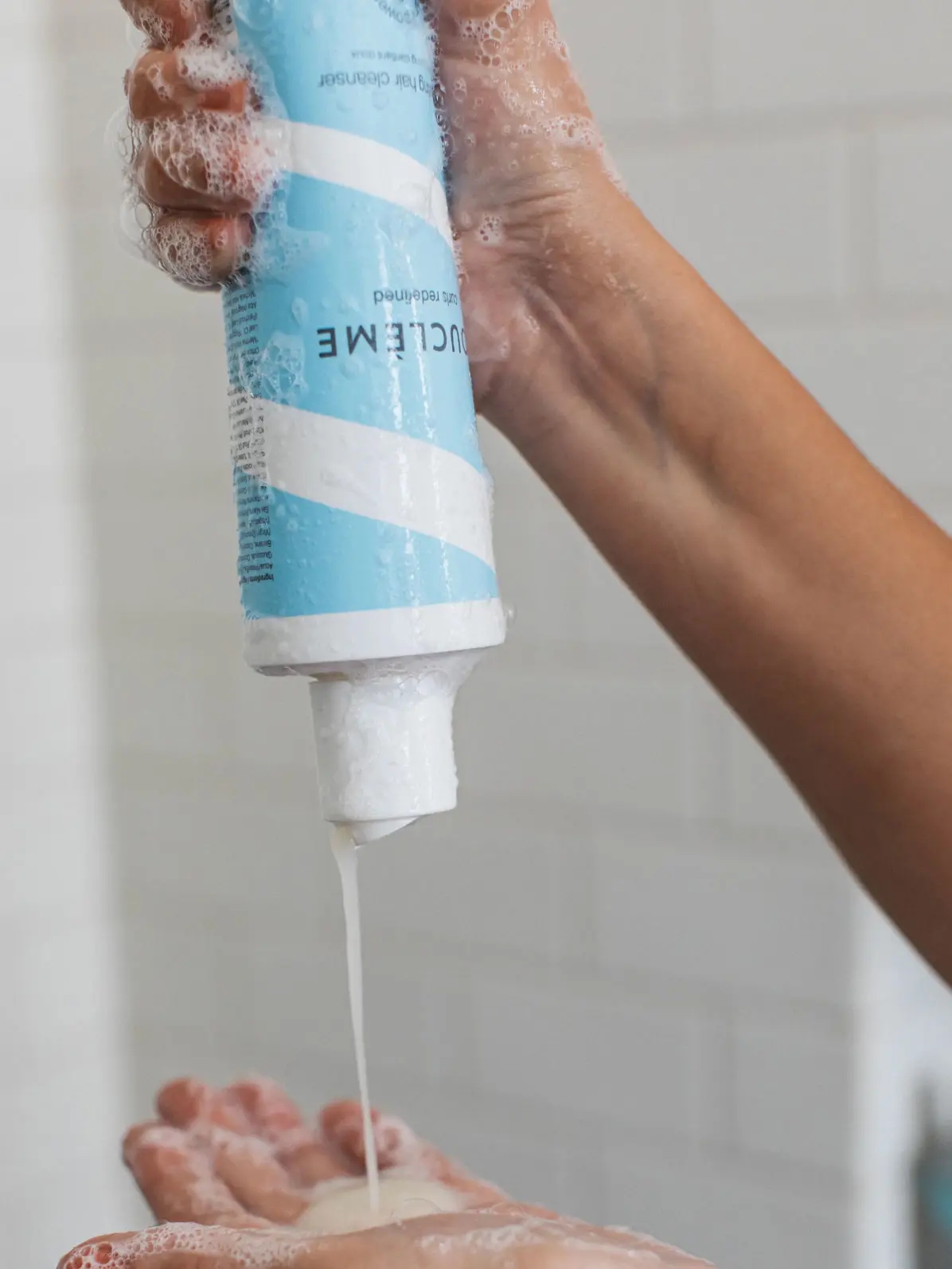Hands squeezing hydrating cleanser in a blue and white bottle