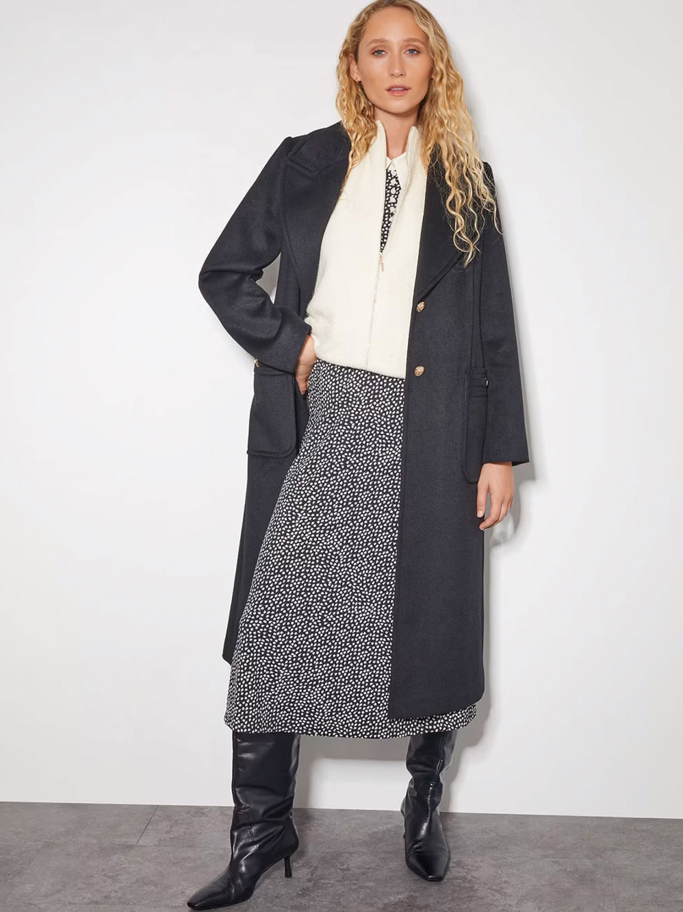 Woman wearing a dress with a coat on top and black boots