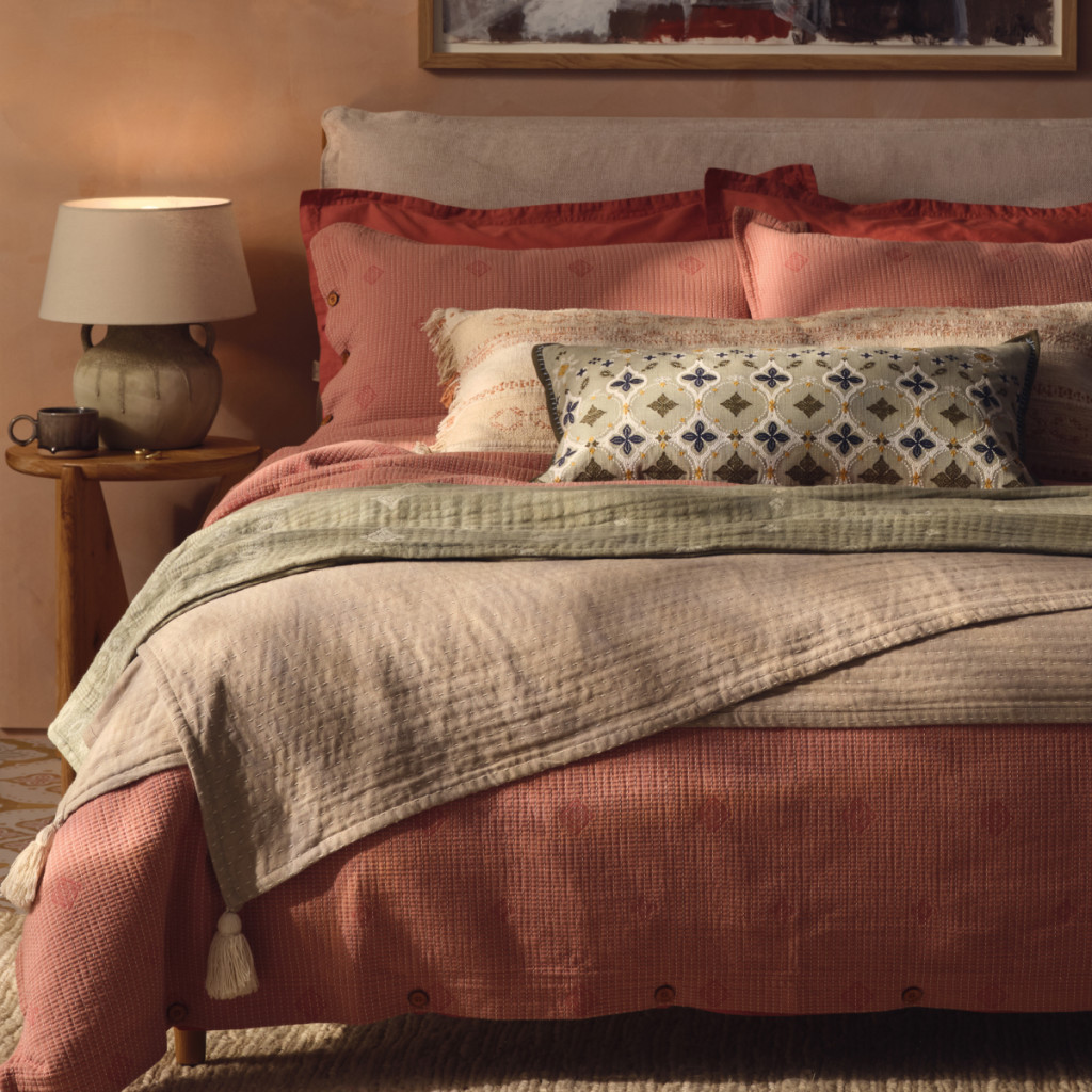 Bed made with earth-toned bedding, pillows and cushions. Read the feature